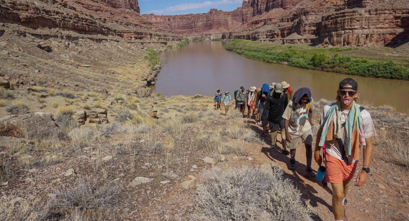 A group of people hike away from a river in a desert landscape